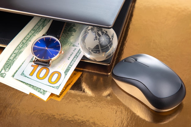 Zegarek na rękę z modelem globu ziemskiego w dolarach w pobliżu laptopa z myszą Biznes online w dowolnym miejscu na świecie Godziny pracy do pracy z laptopem