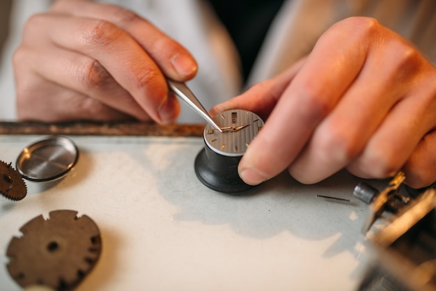 Zegarmistrz naprawia zepsuty mechanizm za pomocą pincety