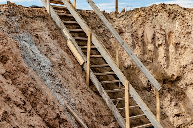 Zejście do głębokiego wykopu podczas budowy budynku Bezpieczeństwo w budownictwie Drabina do zejścia na fundamenty żelbetowe Drabina do sukcesu Drabina drewniana dla pracowników