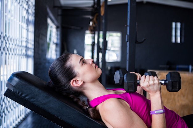 Żeńska atleta trzyma dumbbell podczas gdy kłamający na ławki prasie