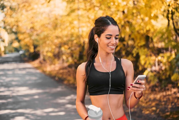 Żeńska atleta uśmiechnięta i patrzeje jej telefon.