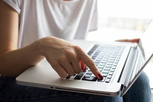 Żeńska ręka pisze na klawiaturze laptopa, naciska klawisz Enter, moment potwierdzenia, zbliżenie