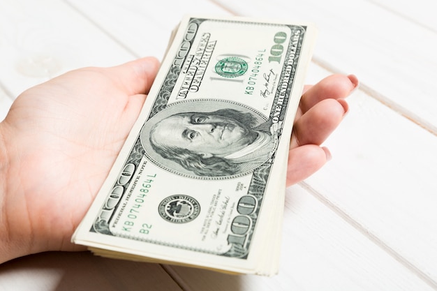 Żeńska ręka trzyma plik pieniądze na drewnianym tle. Widok perspektywiczny sto dolarów banknotów. Koncepcja wynagrodzenia