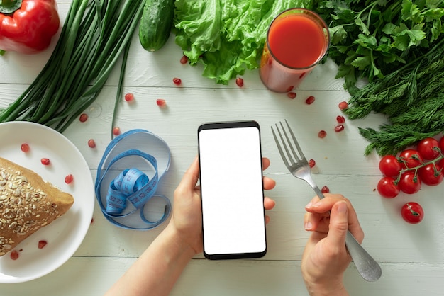 Żeńska Ręka Trzyma Smartphone Na Tle Stół Z Diet Warzywami. Miejsce Na Twój Tekst.