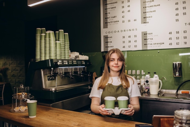 Żeński barista podaje kawę w kartonowych filiżankach