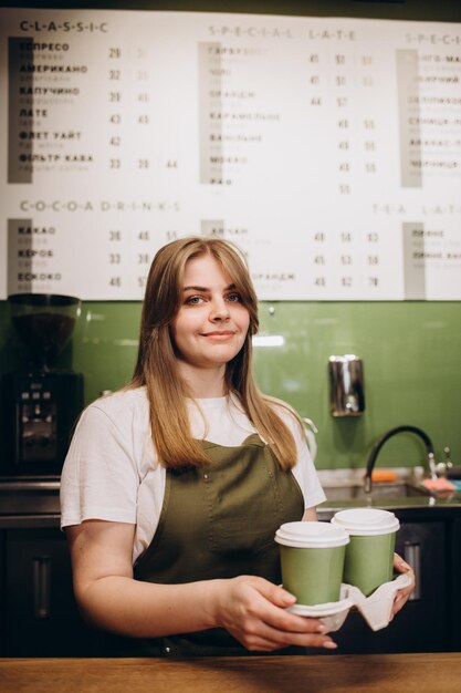 Żeński barista podaje kawę w kartonowych filiżankach