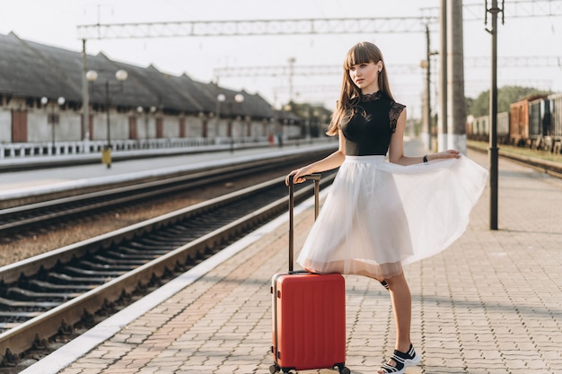 Żeński brunetka podróżnik z czerwonym walizki odprowadzeniem na raiway staci