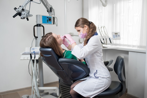 Żeński dentysta z stomatologicznymi narzędziami sprawdza w górę cierpliwych zębów przy stomatologicznym kliniki biurem