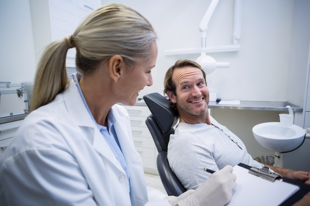 Zdjęcie Żeński dentysty writing na schowku podczas gdy współdziałający z męskim pacjentem