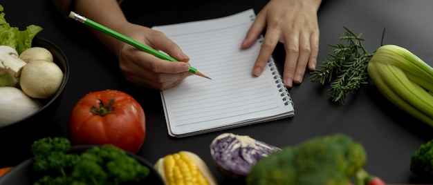 Żeński uczeń bierze przepis notatki na pustym notatniku na czarnym kuchennym stole w kucharstwo klasie