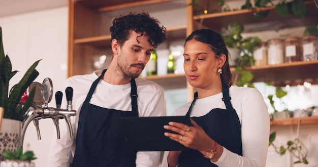 Zespół baristów rozmawia z tabletem w kawiarni mężczyzna i kobieta dyskusja na temat harmonogramu pracy lub kontroli zapasów Technologia komunikacji z systemem online w kawiarni pracującej i zarządzającej sprzedażą