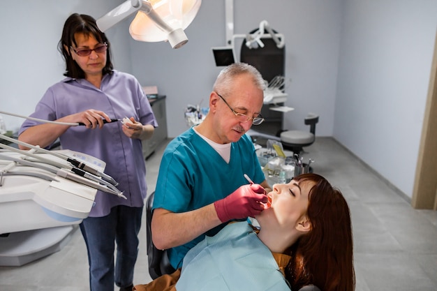 Zespół dentystów, starszy mężczyzna i kobieta oraz młoda pacjentka posiadająca profesjonalne leczenie w nowoczesnym gabinecie stomatologicznym
