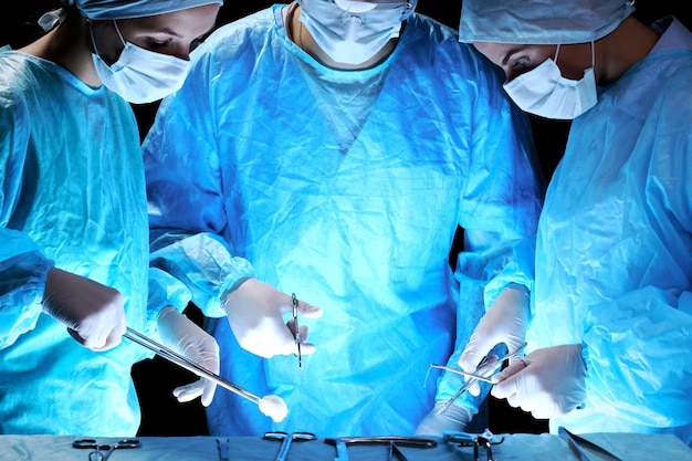 Zespół medyczny wykonujący operację Grupa chirurga przy pracy na sali operacyjnej stonowana na niebiesko
