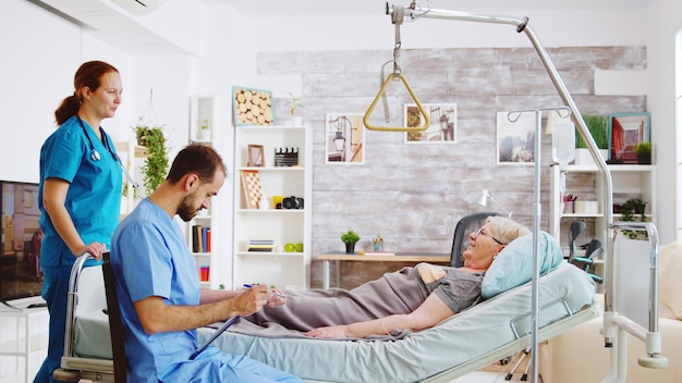 Zdjęcie zespół pielęgniarek i pielęgniarek sprawdzających staruszkę leżącą w szpitalnym łóżku w domu spokojnej starości