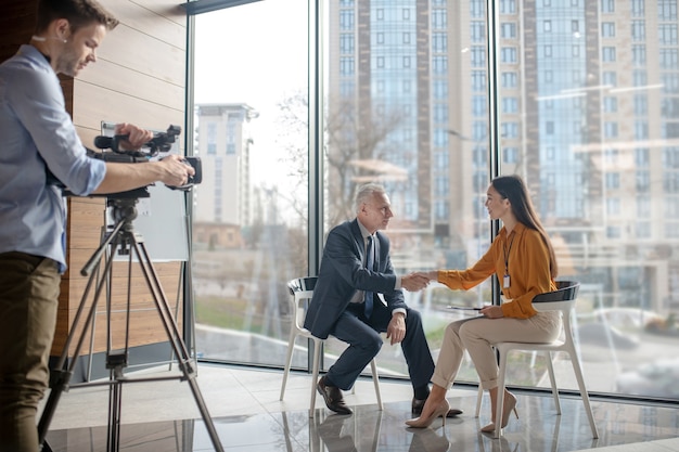 Zespół reporterów pracuje nad rozmową z siwowłosym mężczyzną w studiu