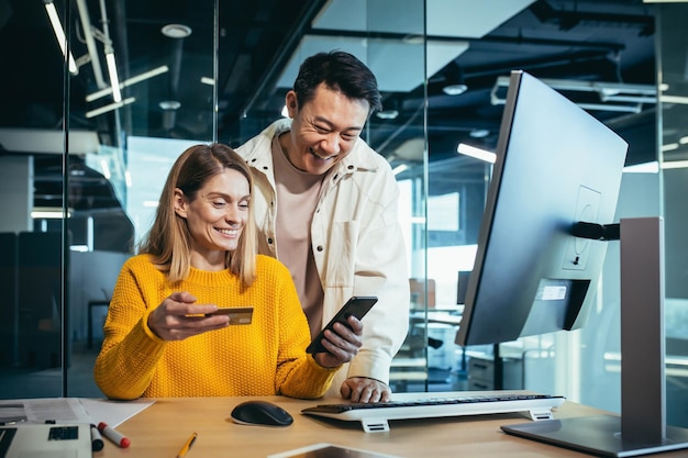 Zespół startupów Azjatycka kobieta i mężczyzna pracują w nowoczesnym biurze, chętnie wybierają i robią zakupy online za pomocą telefonu i bankowej karty kredytowej