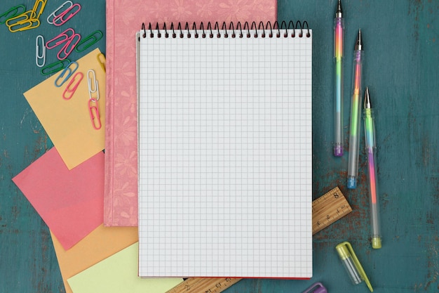 Zestaw biurowy z notebookami, kolorowymi długopisami i przyciskami na niebieskim drewnianym tle
