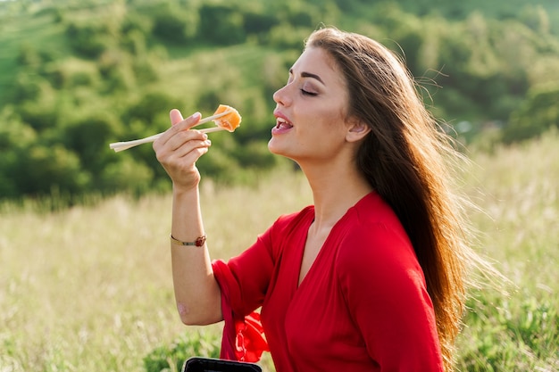 Zestaw Do Sushi I Dziewczyna, Która Wyciąga Rękę, By Gryźć Sushi Na Zielonych Wzgórzach.