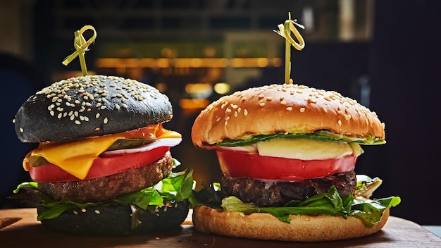 Zestaw domowych hamburgerów w czarno-białe bułeczki z serem sałata pomidorowa cebula na desce do serwowania drewna na ciemnym stole Rustykalny styl Domowe fast foody