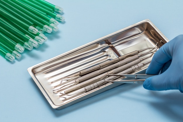 Zestaw instrumentów stomatologicznych do leczenia stomatologicznego oraz ślinociągów. Dłoń dentysty w gumowej rękawiczce z pęsetą. Narzędzia medyczne w tacce ze stali nierdzewnej.