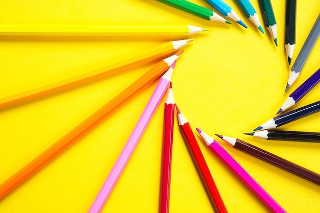 Zestaw kolorowych ołówków na żółtym tle ułożony jest w okrąg w kształcie słońca.