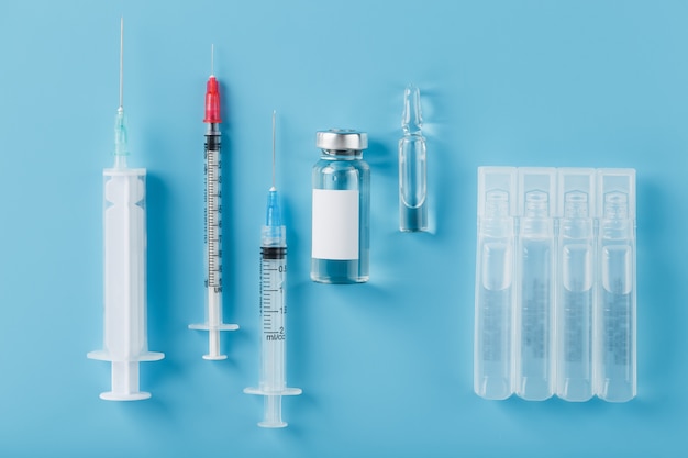 zestaw medycznych strzykawek i ampułek z lekami i szczepionkami z rzędu na niebieskim tle.