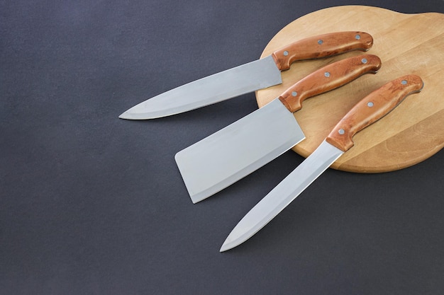 Zestaw profesjonalnych noży kuchennych na desce i ciemnym tle z kopią Zestaw nowoczesnych noży kuchennych