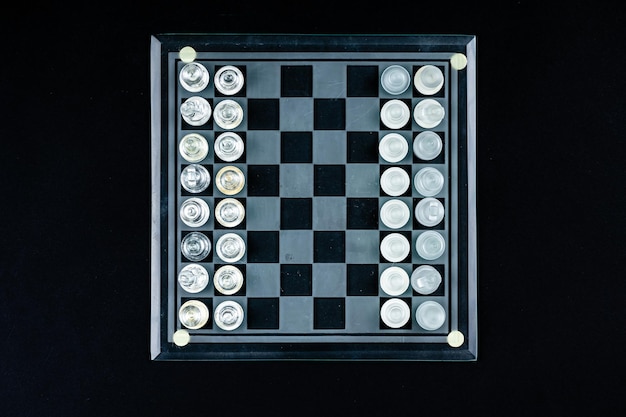 Zestaw przezroczystych szklanych szachów nad czarnym selektywnym widokiem przestrzeni kopii z góry