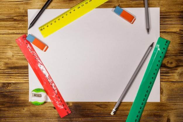 Zestaw przyborów piśmienniczych szkolnych. Czysty arkusz papieru, linijki, ołówki, gumki i temperówka na drewnianym biurku. Widok z góry