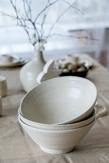 Zestaw pustych, ręcznie robionych białych miseczek ceramicznych stojących na stole z lnianym obrusem i dekoracjami wielkanocnymi.