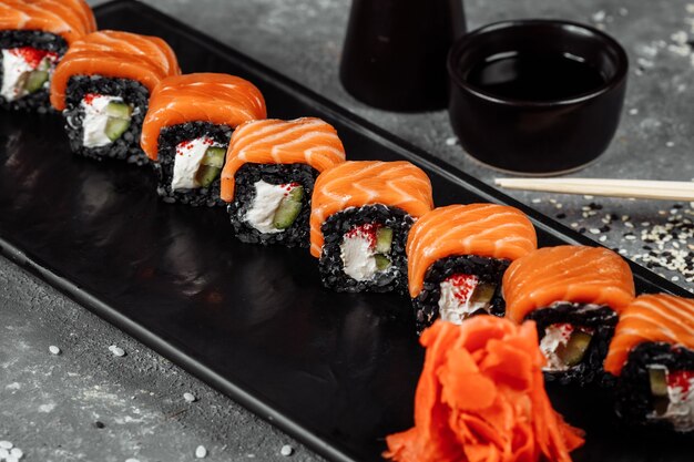 Zestaw Rolek Sushi Philadelphia Z Czerwoną Rybą, Twarogiem I Czarnym Ryżem Leży W łódce Z Talerza. Rolki Sushi Na Szarym Tle.