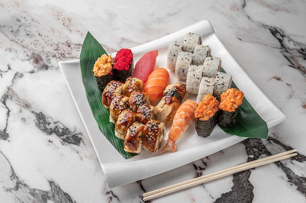 Zestaw różnych kolorowych maki sushi rolls nigiri i gunkan z krewetką tygrysią tomago łososiem sałatką z tuńczykiem chuka latająca ryba kawior tuńczyk i zielony liść bambusa w białym ceramicznym talerzu widok z boku