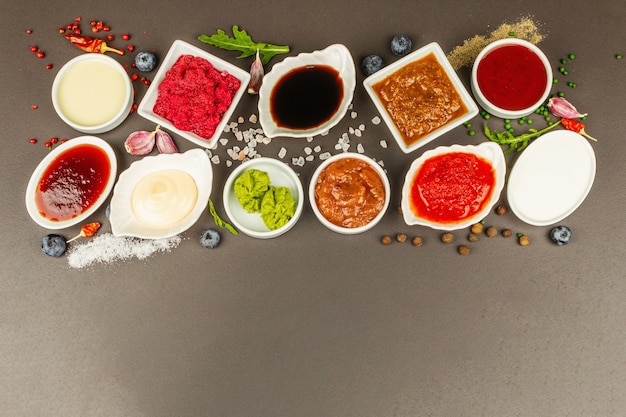 Zestaw różnych sosów - ketchup, majonez, barbecue, sojowy, chutney, wasabi, adjika, chrzanowy, aioli, marinara. Ciemne kamienne tło betonowe, widok z góry