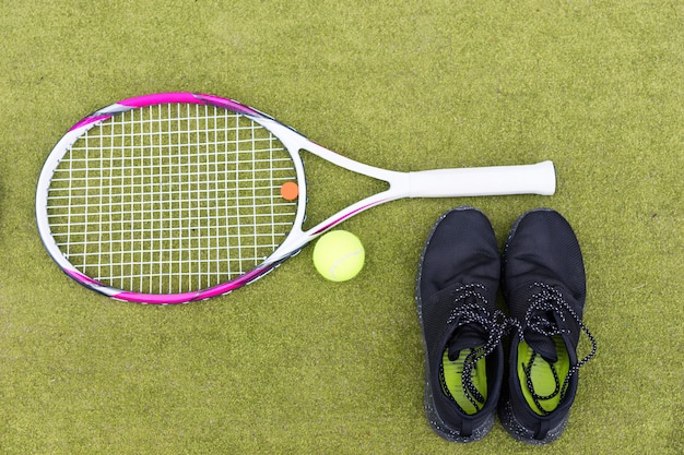 Zestaw sprzętu tenisowego rakieta tenisowa, piłka i trampki męskie na boisku z zielonej trawy