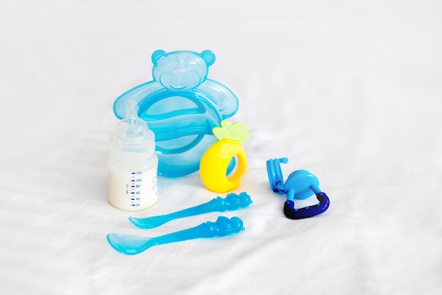 Zestaw zastawy stołowej dla niemowląt butelka mleka do karmienia nibbler niebieskie sztućce łyżka widelec pieluchy zabawki jednorazowe pieluchy na białym tle łóżka
