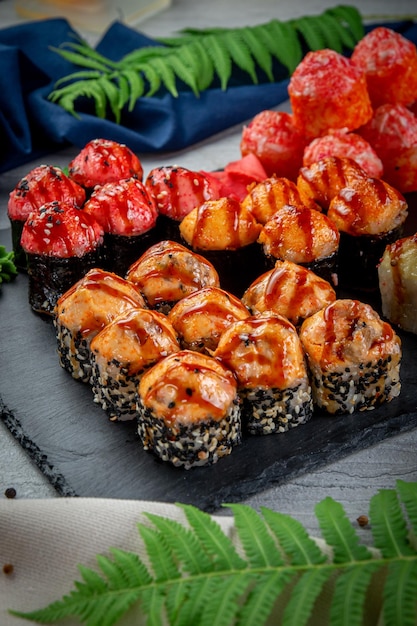 Zdjęcie zestaw ze smażonymi i pieczonymi rolkami sushi na kamiennej desce na lekkim stole