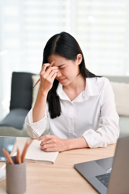 Zestresowana azjatycka bizneswoman zaniepokojona terminem realizacji projektu, boryka się z bólem głowy