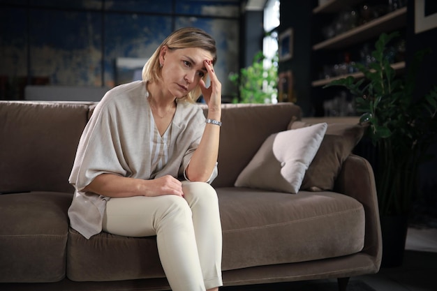 Zestresowana kobieta w średnim wieku siedzi na kanapie w salonie pogrążona w myślach