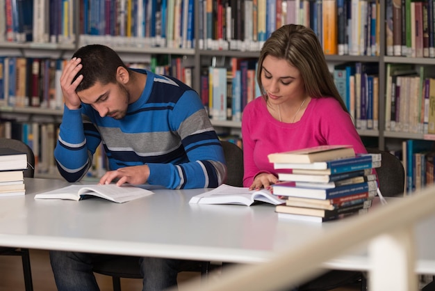 Zestresowani uczniowie liceum siedzący przy biurku w bibliotece Płytkiej głębi ostrości