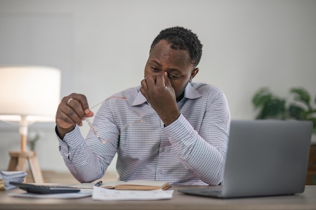 Zestresowany biznesmen siedzący w biurze Zmęczony i przepracowany murzyn Młodzi afrykańscy wyczerpani mężczyźni w stresie pracujący na laptopie