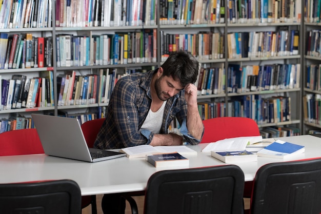 Zestresowany młody student czytający podręcznik siedząc w bibliotece