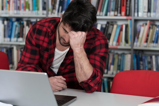 Zestresowany młody student czytający podręcznik siedząc w bibliotece