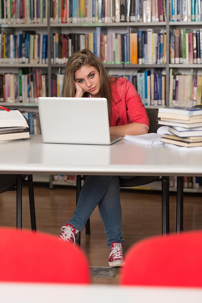 Zestresowany uczeń liceum siedzący przy biurku w bibliotece Mała głębia ostrości