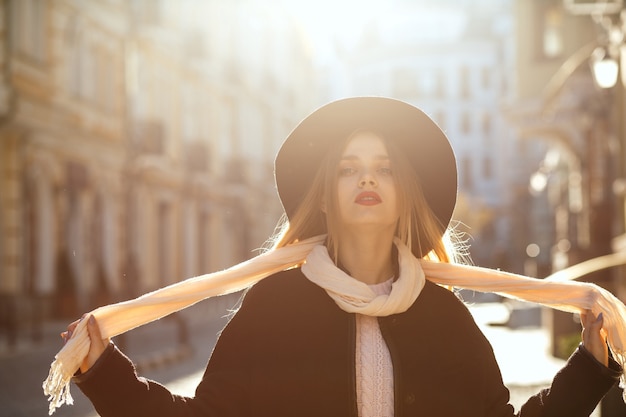 Zewnątrz portret chwalebnej blondynki kobiety na sobie kapelusz, szalik i płaszcz, pozowanie na starej ulicy w blasku słońca. Miejsce na tekst