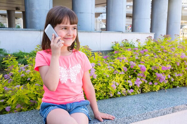 Zewnątrz Portret Dziewczyny 67 Lat Rozmawia Przez Telefon W Mieście Na Tle Kwiatów. Wesołe Dziecko