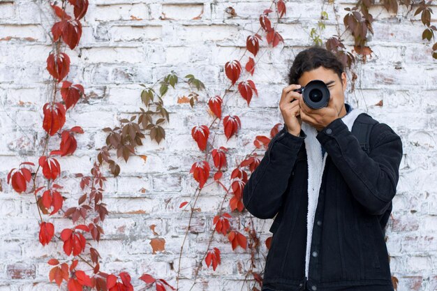 Zewnątrz ujęcie młodego mężczyzny w czarnym płaszczu z aparatem dslr w dłoniach