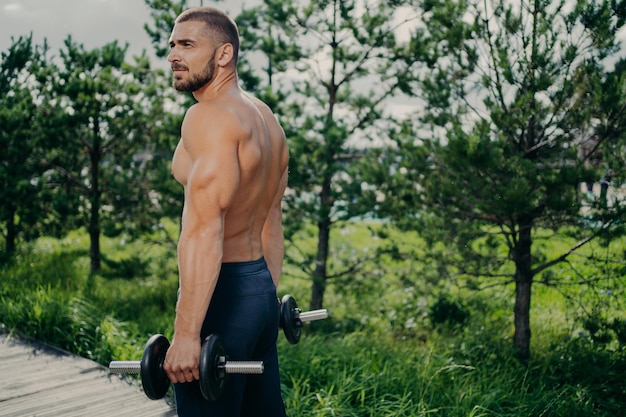 Zewnątrz ujęcie muskularnego silnego mężczyzny przygotowuje się do treningu ze sztangą podnosi ciężary i pozy na ulicy daje motywację wszystkim Męski sztangista wykonuje ćwiczenia bicepsów nosi sportowe ubrania
