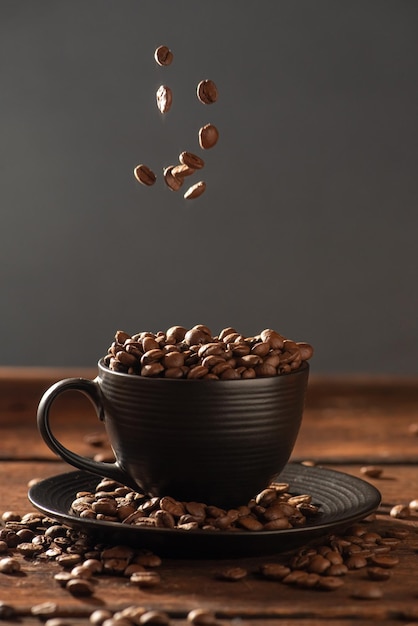Ziarna kawy i czarny kubek spadające ziarna kawy do czarnego kubka na rustykalnym drewnie ciemne jedzenie w stylu fotografii selektywnej ostrości