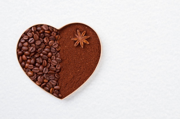 Ziarna kawy i proszek w kształcie serca. Na białym tle na białej powierzchni