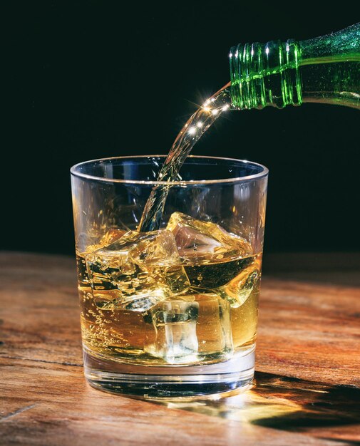 Zielona butelka whisky w kryształowej szklance z kostkami lodu na drewnianym stole